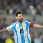 Argentinian soccer captain in a blue-and-white jersey with number 10 celebrates with arms outstretched on the pitch.