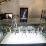 Glass display case holding a row of curved-blade daggers on clear stands in a museum exhibit set-up.