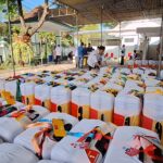 Rows of ready-to-distribute gift bags under a canopy at an outdoor community event; volunteers organizing them.