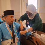 Healthcare worker in a hijab checks an elderly man's blood pressure with a cuff at a health event set-up in a conference area.