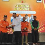 Man in a white shirt hands an award envelope to a delivery rider in an orange Shopee Food uniform on a stage during a national seminar.