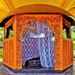 Ornate wooden pavilion with open carved doors and a waterfall feature inside, set in a tropical garden.