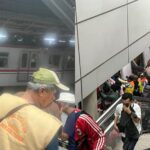 Split image: left side shows a man in a beige jacket and green cap on an escalator beside a stationary subway train; right side shows a crowded metro platform with many people and a blue sign reading '1 Cikarang'.