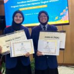 Two female students in blue blazers pose with certificates at a ceremony, smiling in front of a blue event screen and flags.