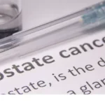 Close-up of a syringe and vial resting on a document that reads 'Prostate cancer'—suggesting medical research or treatment context.