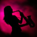 Silhouette of a saxophonist playing on stage with pink fog behind them.