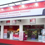 Front view of Koperasi Desa Merah Putih store with a red sign, open entrance, and customers shopping inside.