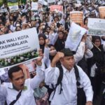 Large crowd of protesters marching in white clothing, holding placards including 'PAK WALI KOTA TASIKMALAYA'