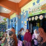Colorful indoor entrance to a kids' activity area with banners and decorative hanging ornaments, people in batik clothing waiting in line.