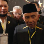 Group of people at a formal event; central older man in a black cap speaks as others photograph him with phones.