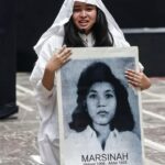 Young woman in white clothes holding a large portrait of Marsinah at a protest rally