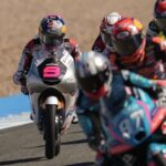 Motorcycle racers on a track in a close chase, rider with pink number 5 leading the pack on a silver bike.