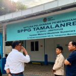 Five people stand outside a teal signboard building that reads SPPG TAMALANRE A 14, a government service center in Indonesia.