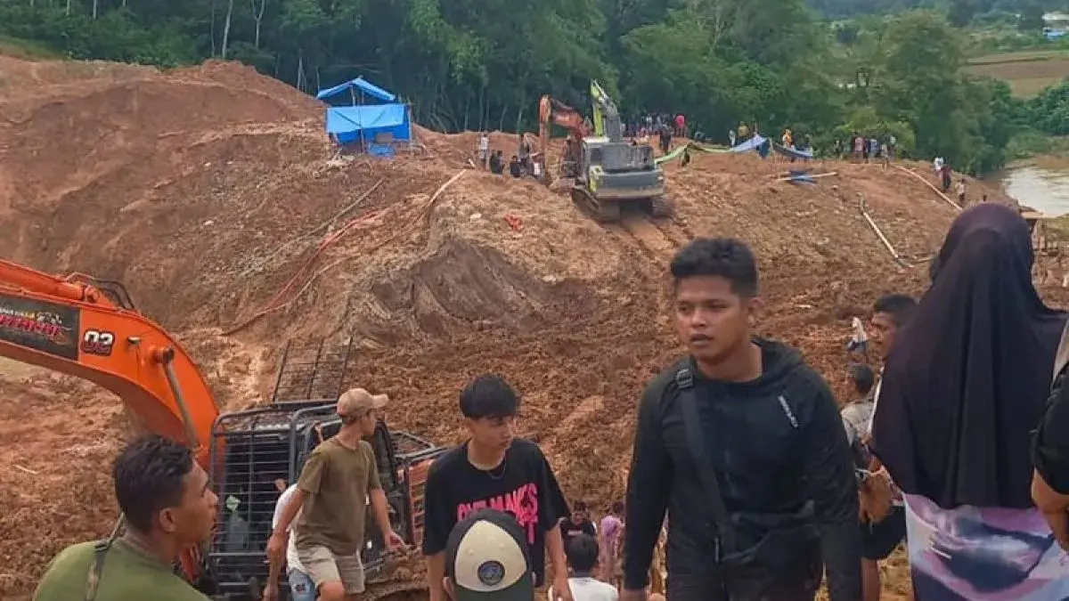 Construction site on a muddy slope with an orange excavator and workers; crowd visible in the background on the hill carven by earthworks.
