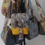 Assorted patterned handbags hanging on a display stand, including a yellow front bag with a marble flap.
