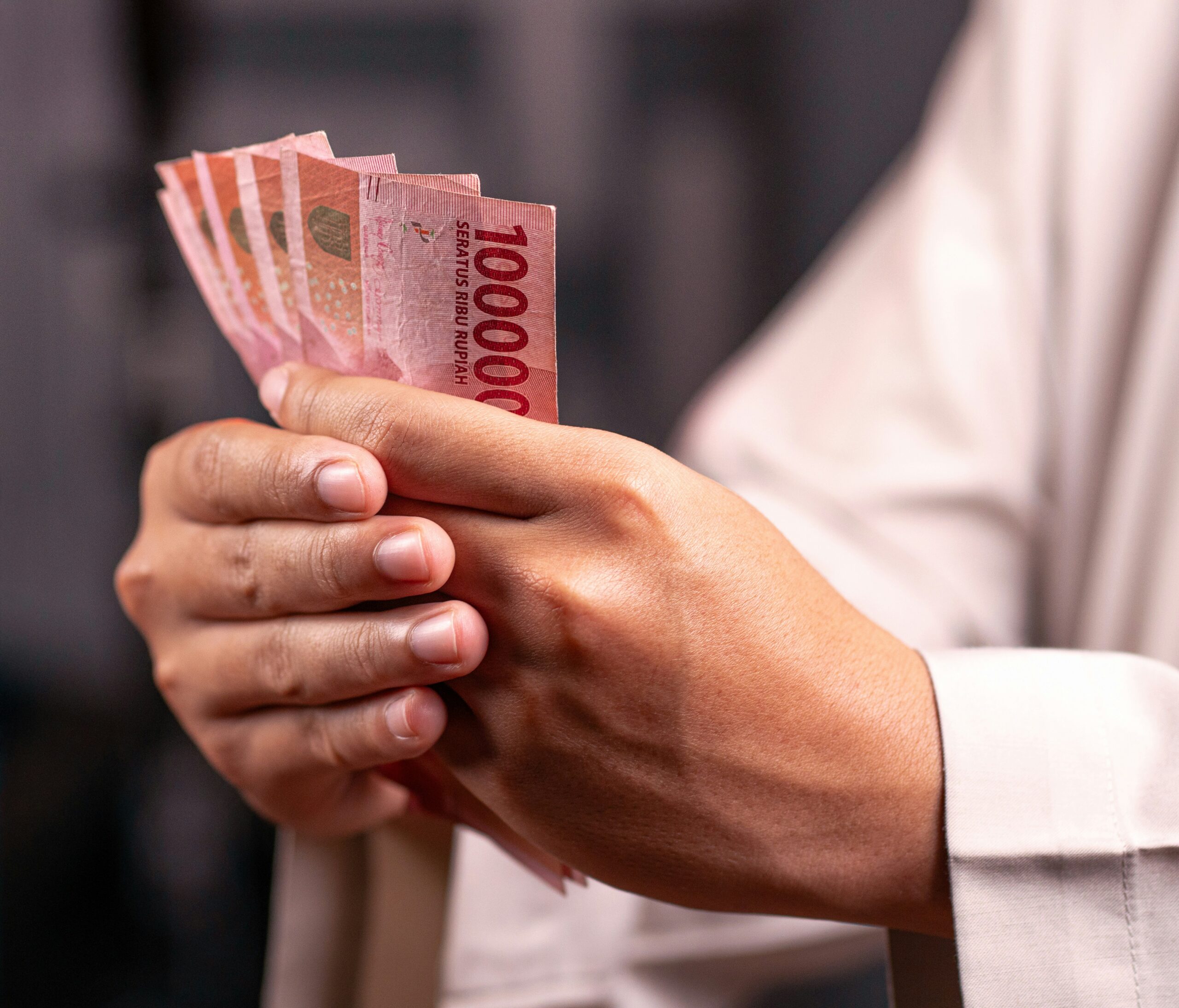 A person holding a fanned stack of red 1,000 rupiah banknotes between their fingers.