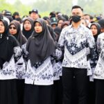 Crowd of people wearing matching black-and-white batik uniforms, including hijab-clad women, at an outdoor event.