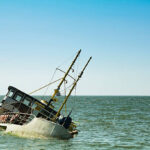 Sunken boat partially submerged in calm blue-green water near the horizon, tilted to one side.