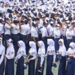Large group of students in white shirts and navy uniforms standing in rows for a school assembly outside.