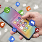 Person holds a smartphone with colorful social media app icons floating around the screen labeled 'Social Media'.