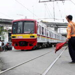 Train paused on tracks as a uniformed railway worker signals with a red flag beside the rails.