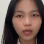 Young woman speaks directly to the camera against a light background, likely recording a video message or vlog.