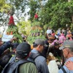 Crowd of people at an outdoor festival gathered around two tall towers made of leaves and vegetables.