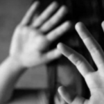 Black-and-white photo of a person raising their hands to shield their face, conveying distress or fear.