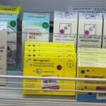 Shelf of pharmaceutical boxes on a store shelf, including Aloclar Plus Mouthwash (white boxes), blue Termorex/Relco items, and bright yellow Microgynon boxes, suggesting a pharmacy display.